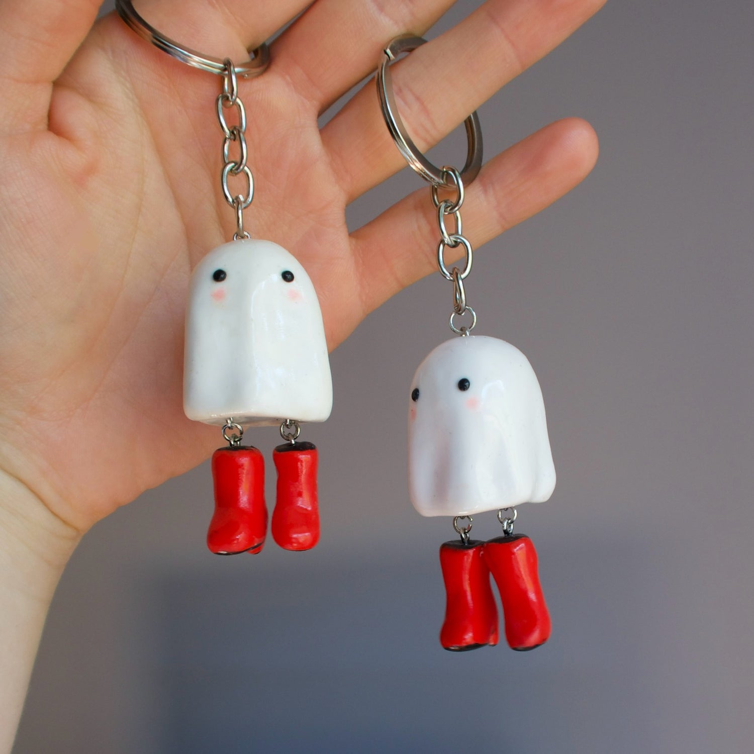 Two ghost keychains with red boots held in a hand against a gray background